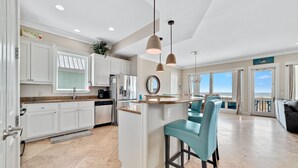 A modern kitchen with white cabinetry, a central island, and bar stools. - Lone Palm by GSVR | Charming Beachfront Retreat w/ Great Primary Bed/Bath + FREE Activities/Golf (Gulf Shores)