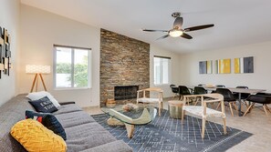 Een moderne woonkamer met een stenen open haard, een eethoek met een tafel en stoelen, en een plafondventilator.