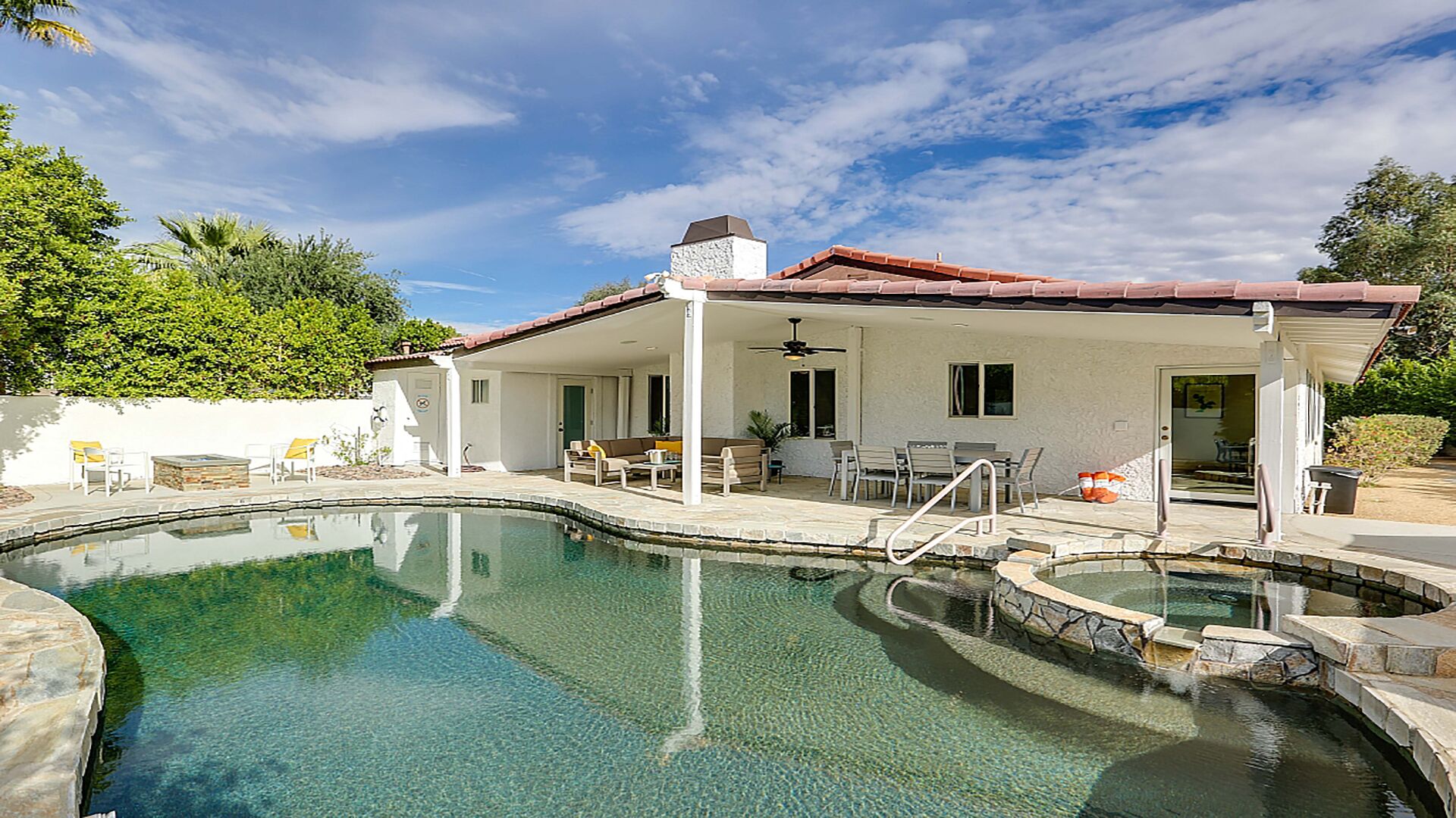 A swimming pool with a patio area, a covered seating area, and a stone wall.
