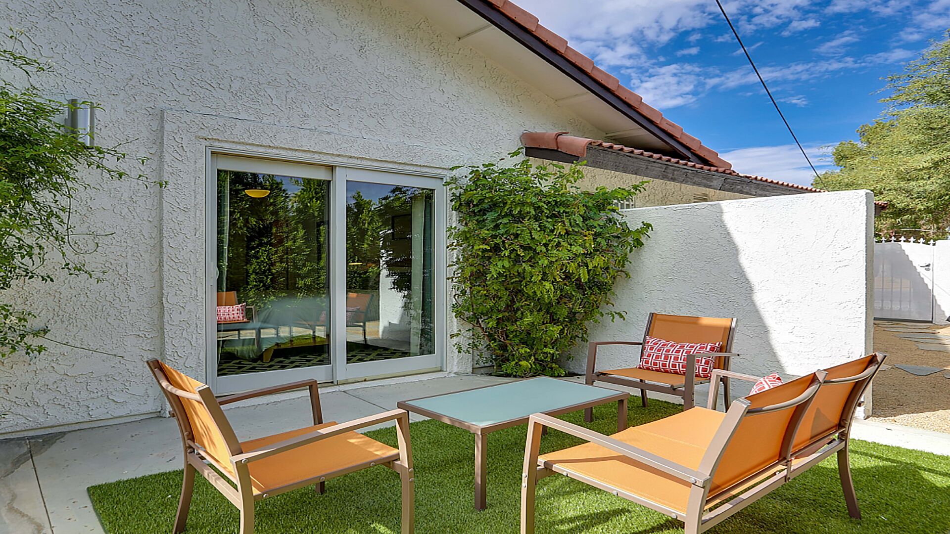 A patio with a table and chairs, a sliding glass door, and a white wall with a red roof.
