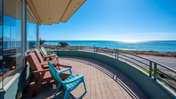 A wooden deck with chairs overlooking a beach and ocean.