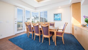 A dining area with a table and chairs, a view through glass doors, a painting, and a kitchen area with cabinets.