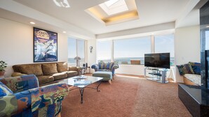 A spacious living room with a large window, a ceiling skylight, a flat-screen TV, and a comfortable seating area.