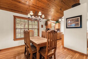 A dining area with a wooden table and chairs, a chandelier, and a view of the outdoors through a window. - Rustic and Quaint, Pet Friendly Cabin. Tucked Away In Gorgeous Stonebridge! (Branson West)