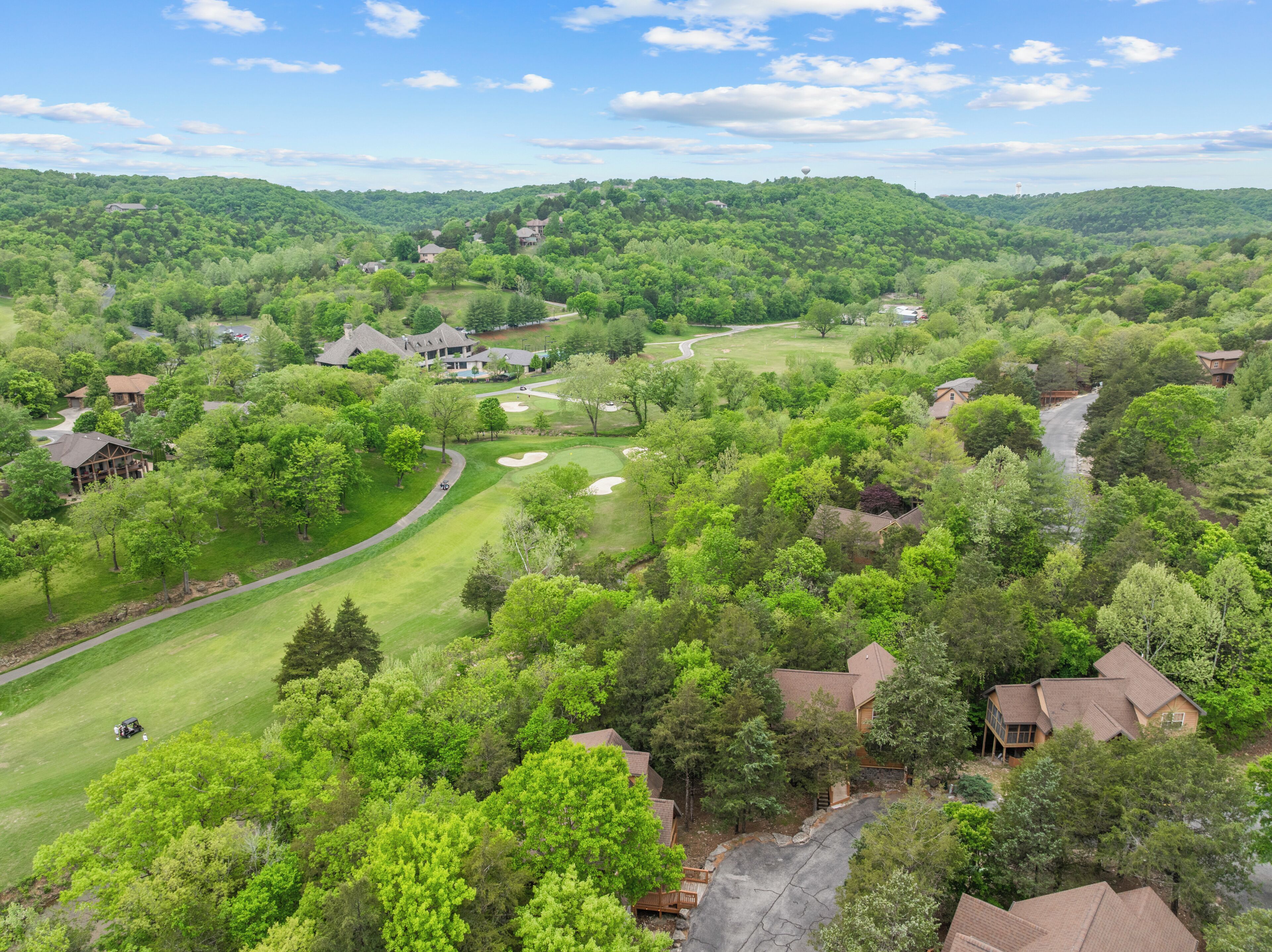 A golf course with multiple houses and a large building, surrounded by dense green trees.