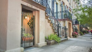 Une rangée de maisons de ville avec une façade en pierre, un portail en métal et des plantes en pot sur le trottoir.