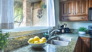 Une cuisine dotée de plans de travail en granit, d’un évier en acier inoxydable, de meubles en bois et d’un saladier rempli de citrons.