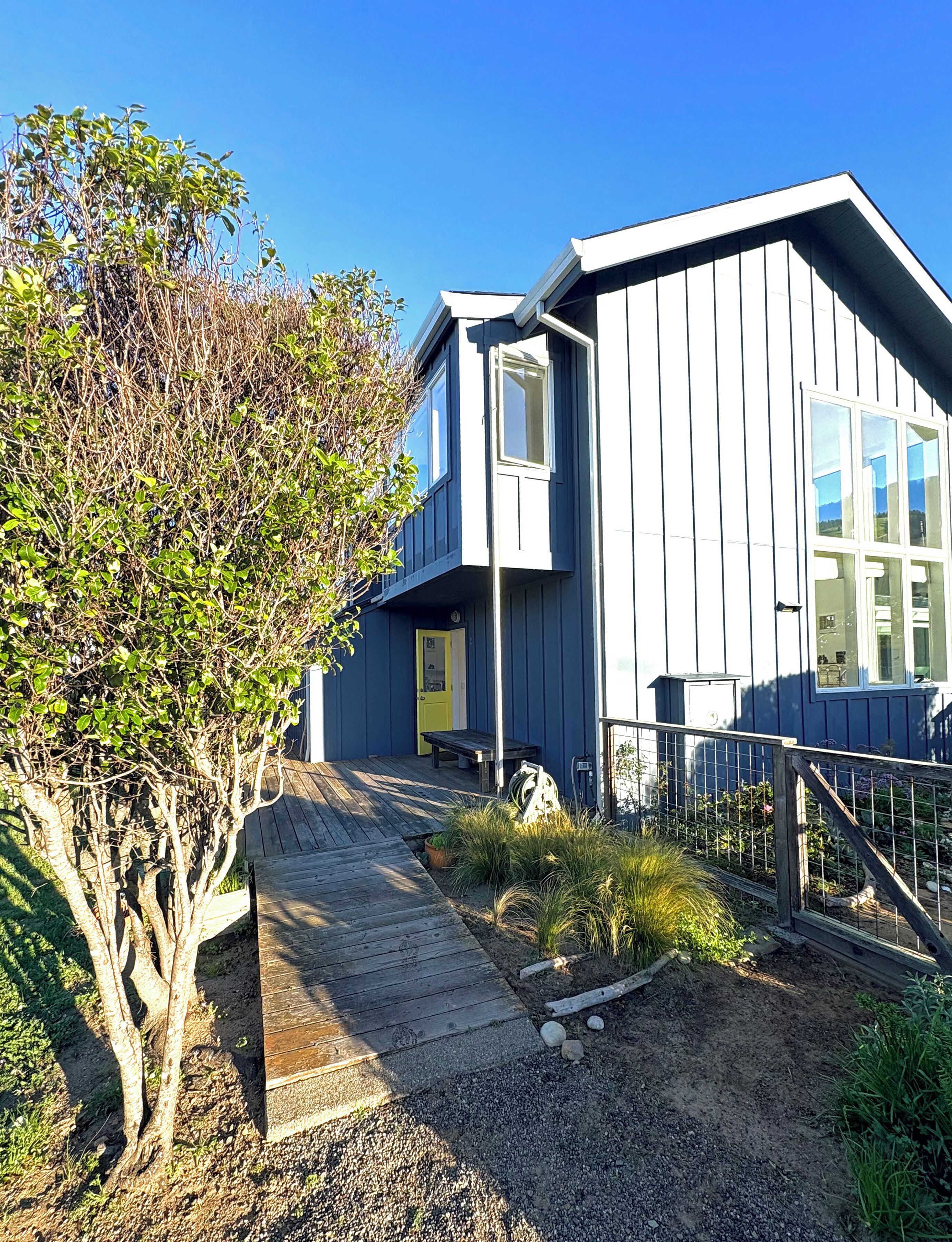 A modern house with a wooden deck, a small garden, and a clear blue sky.