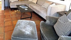 A living room with a sofa, ottoman, and armchair, a coffee table, and a painting on the wall. - Steps From the Beach, Private Yard, Hot Tub (Stinson Beach)