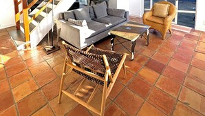 A living room with a sofa, a wicker chair, a coffee table, a staircase, and a view through a glass door. - Steps From the Beach, Private Yard, Hot Tub (Stinson Beach)