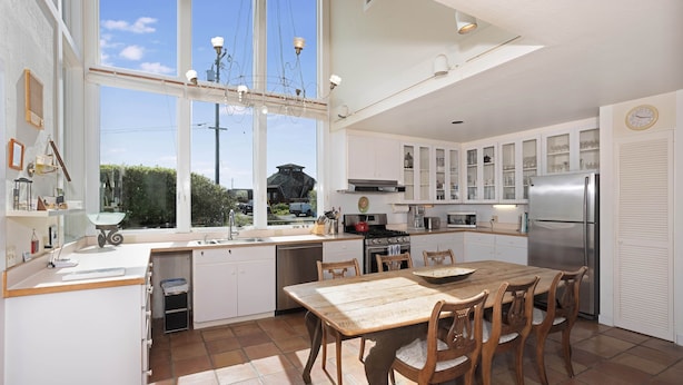 A modern kitchen with white cabinetry, a large island, and a view of the outdoors. - Steps From the Beach, Private Yard, Hot Tub (Stinson Beach)