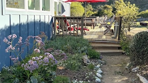A building with large windows, a deck with outdoor seating, and a garden path. - Steps From the Beach, Private Yard, Hot Tub (Stinson Beach)