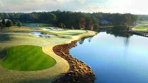 Ein Golfplatz mit Bunkern, Wasserhindernissen und einem Clubhaus im Hintergrund.