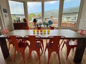 A dining area with a large table, red chairs, and a view of a mountainous landscape through large windows.