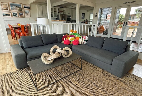 Un salon moderne avec un canapé d’angle gris, une table basse en fibres tressées et une collection de peluches.