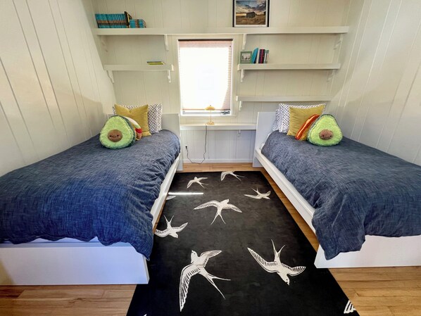 A bedroom with two beds, a window, and a bookshelf. - Fresh and Lovely Inner Lagoon Home (Stinson Beach)