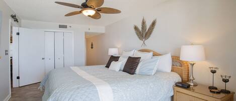 A bedroom with a bed, a ceiling fan, two bedside lamps, a decorative wall piece, and a wicker nightstand.