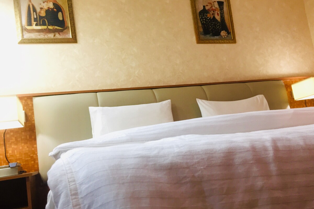 Una habitación de hotel con una cama grande, dos mesitas de noche y dos lámparas de pared.