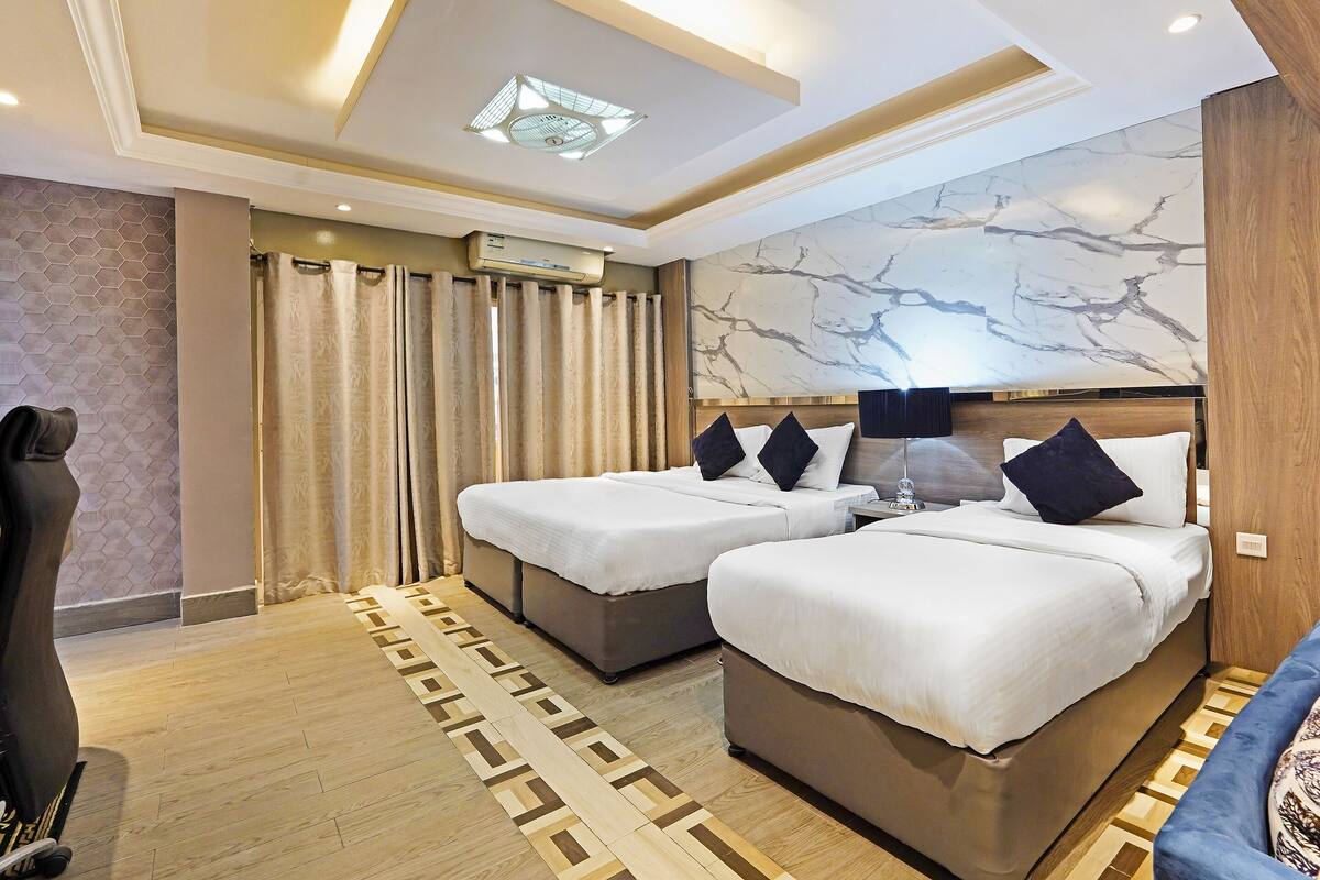A hotel room with two beds, a ceiling fan, a marble wall, and a patterned rug.