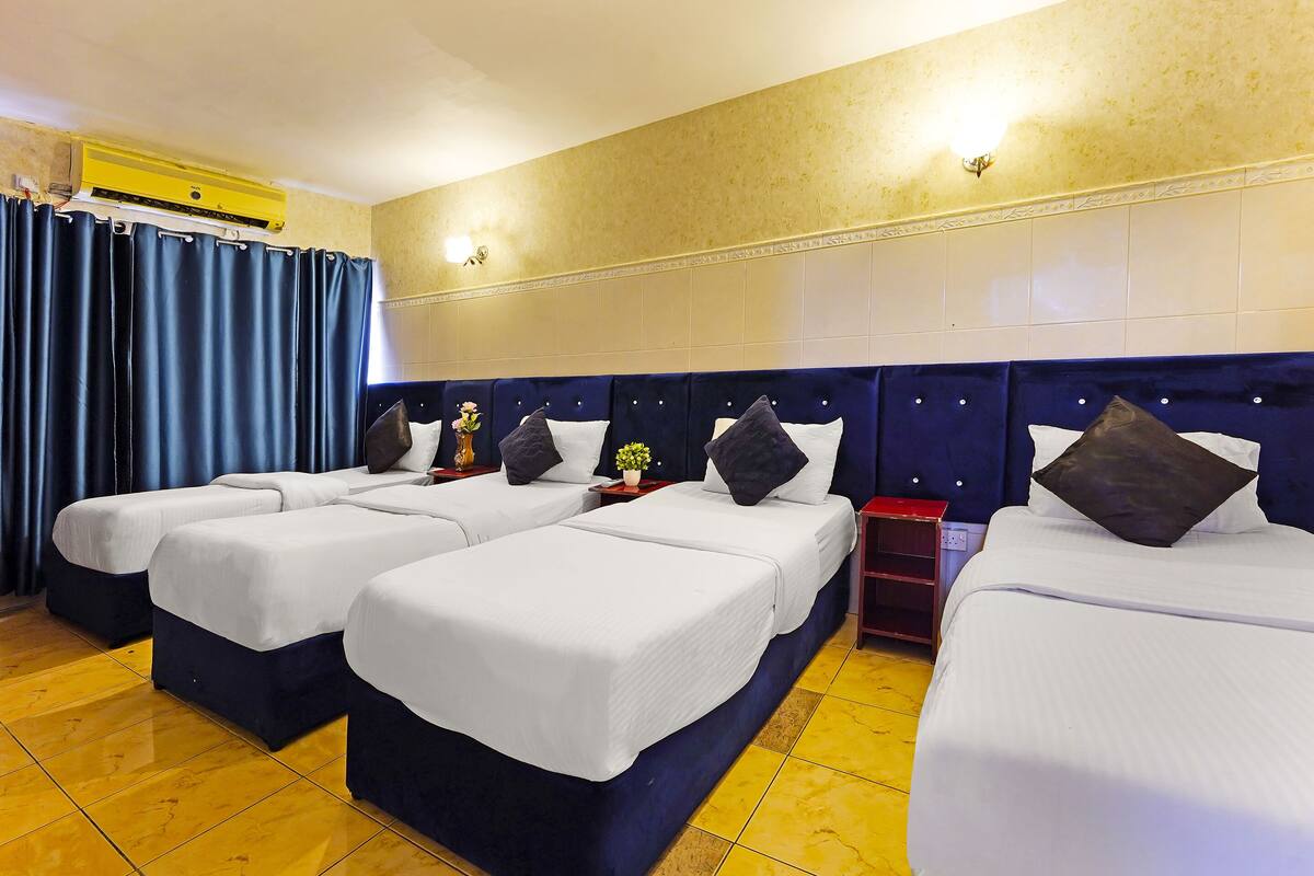 A hotel room with four beds arranged in a row, a ceiling air conditioner, and a decorative wall light.