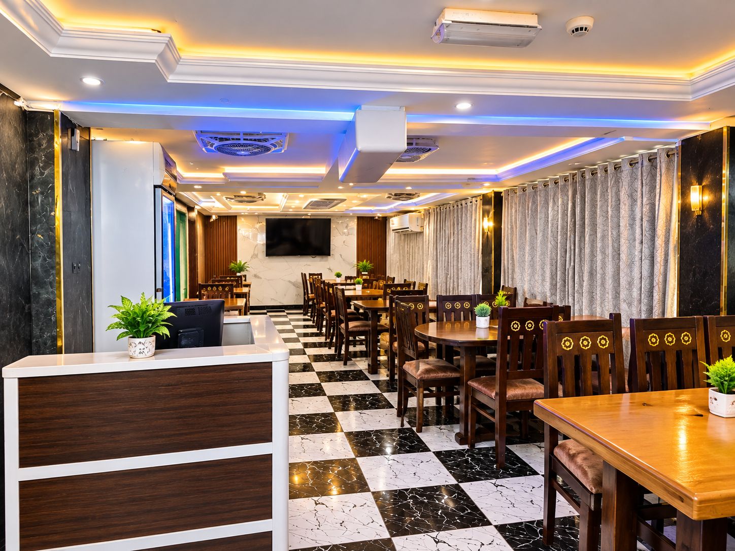 Un vestíbulo de hotel con piso a cuadros, muebles de madera, una mesa de recepción y un televisor de pantalla plana montado en la pared.
