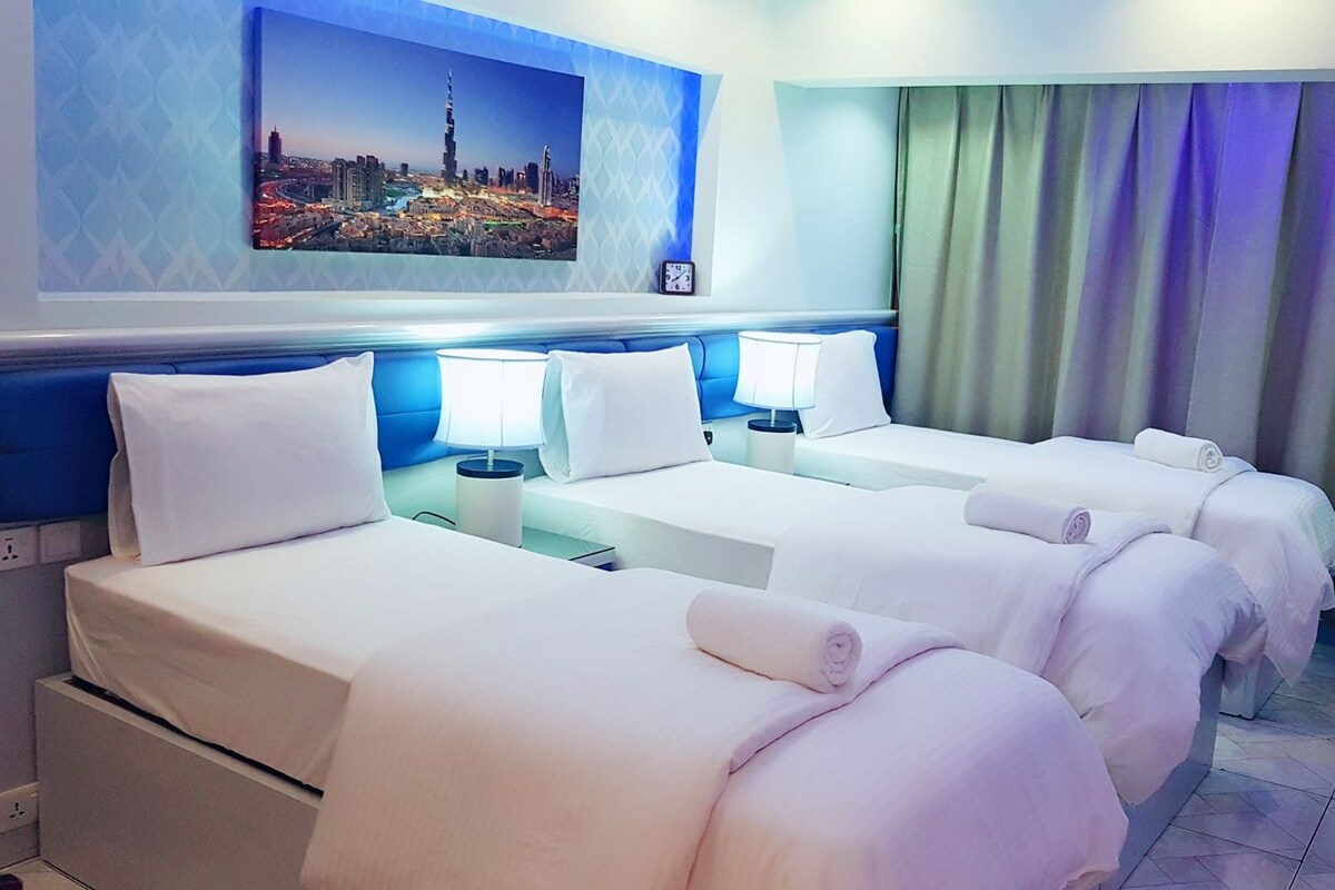 Habitación de hotel con tres camas, vista a la ciudad, un reloj y una cortina.