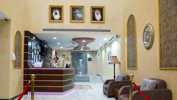 Een hotel lobby met een receptiebalie, een zithoek en portretten in lijsten aan de muren.