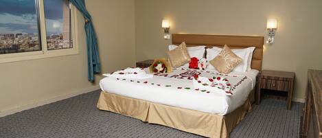 A hotel room with a large bed, two bedside tables, a nightstand, a window with curtains, and a cityscape view.