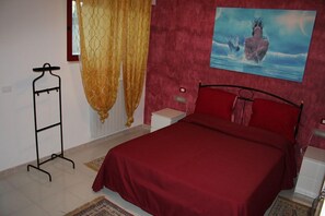 A bedroom with a bed, a nightstand, a wall-mounted lamp, a window with curtains, and a painting. - Le Sirene Bed and Breakfast (Cellamare)