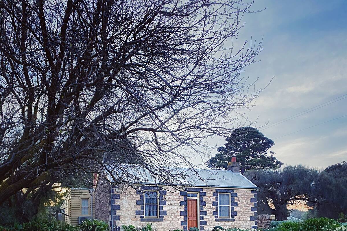 A stone house with a red door, surrounded by a well-maintained lawn and various flowering plants.