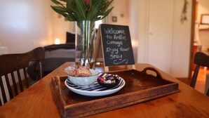 A wooden table with a tray holding a bowl of biscuits and a small bowl of candies. A vase with flowers and a welcome sign are also visible. - Cherry Plum Cottages (Port Fairy)