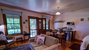 A cozy living room with a sofa, a dining table, and a kitchen area with a microwave. - Cherry Plum Cottages (Port Fairy)