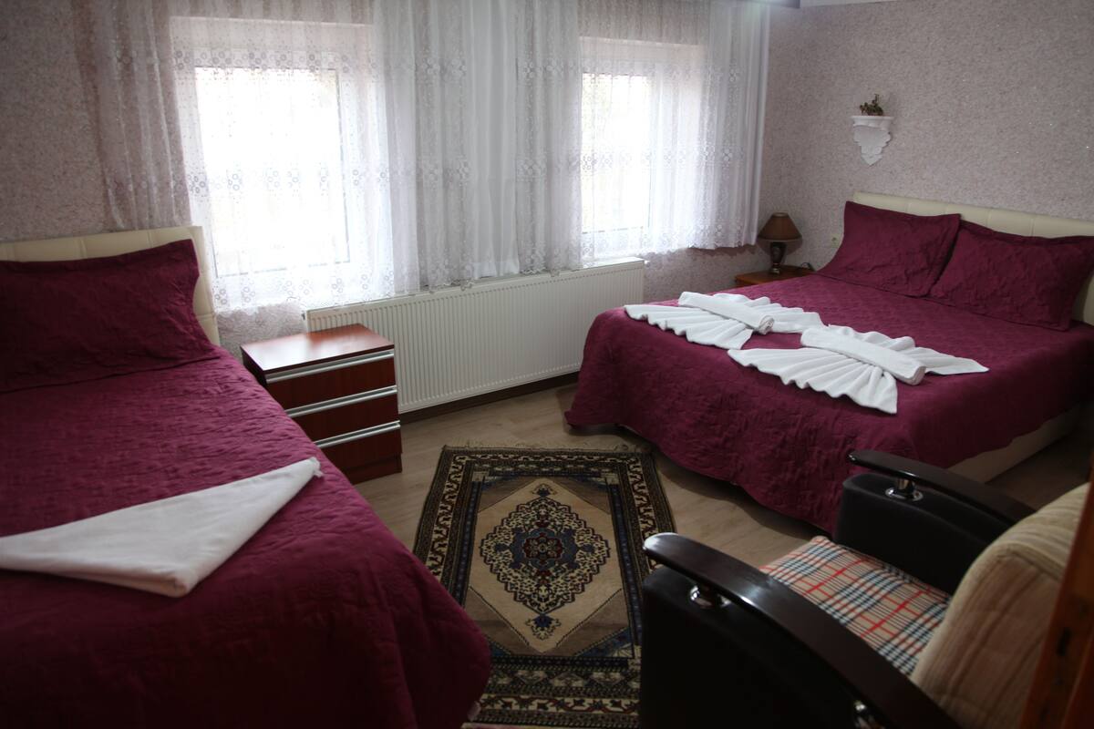 Ein Hotelzimmer mit zwei Betten, einem kleinen Tisch, einem Stuhl und einem Fenster mit durchsichtigen Vorhängen.