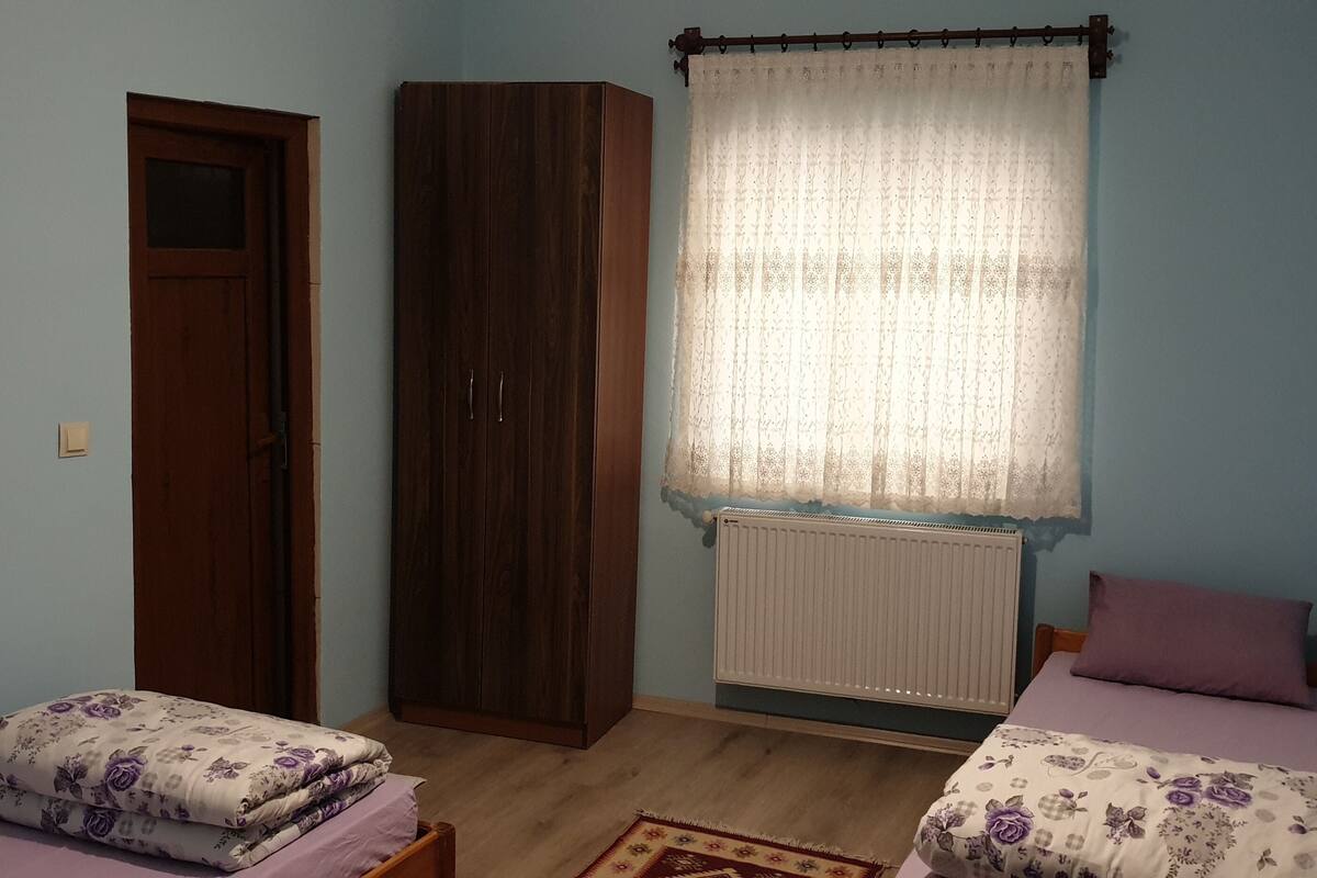 Ein Schlafzimmer mit zwei Betten, einem Kleiderschrank, einem Heizkörper und einem Fenster mit Vorhang.