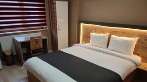 Una camera d'albergo ordinata con un letto grande, una testiera in legno, una scrivania con una sedia e un termosifone.