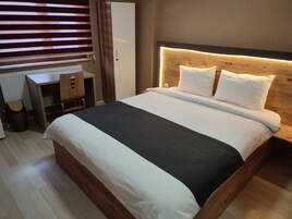 A neatly arranged hotel room with a large bed, a wooden headboard, a desk with a chair, and a radiator.