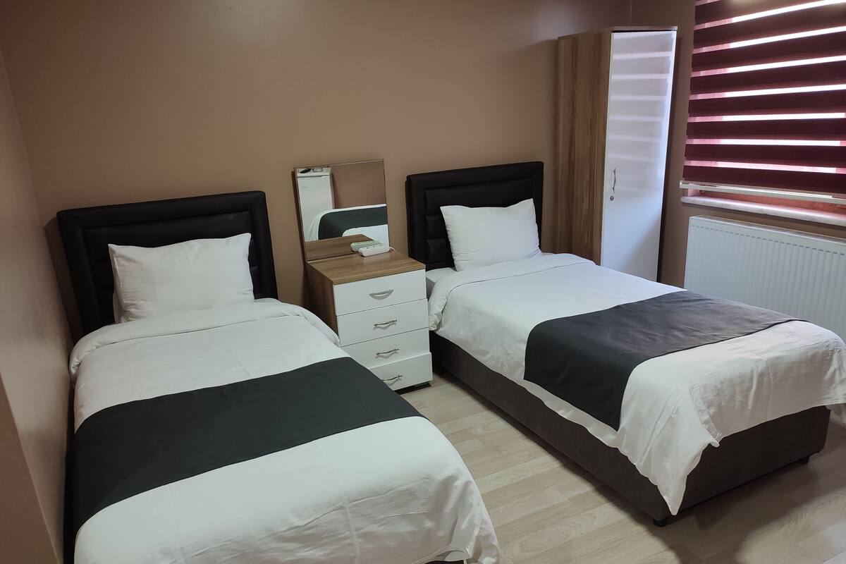 Ett hotellrum med två separata sängar, en byrå, en spegel och ett fönster med persienner.