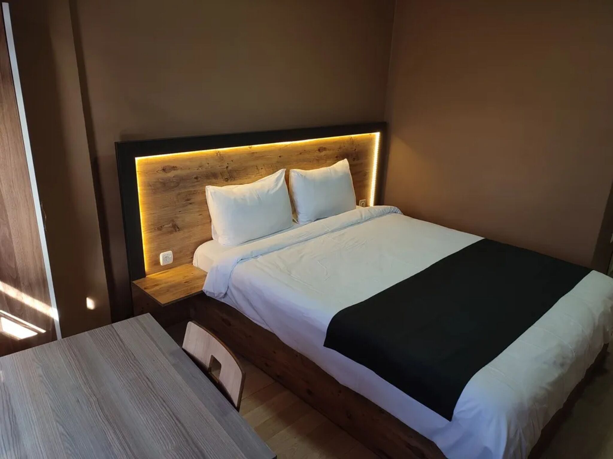 A neatly made bed with white and black bedding, a wooden headboard, and a bedside table with a lamp.