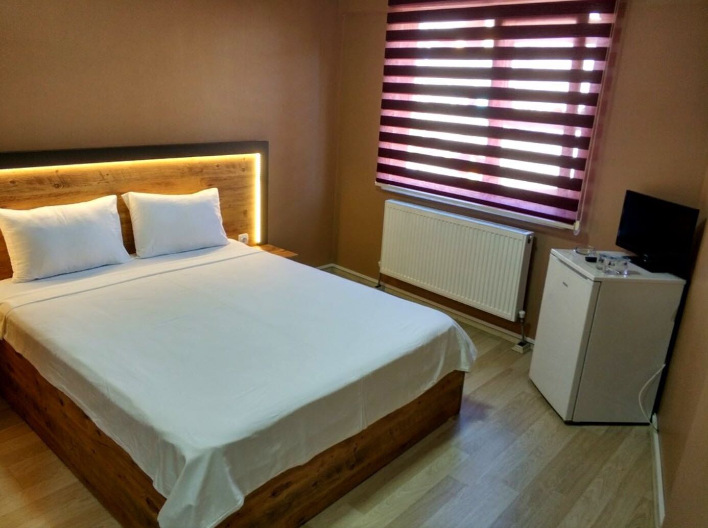 Une chambre à coucher avec un lit, une petite armoire blanche, un radiateur et une fenêtre avec des stores.