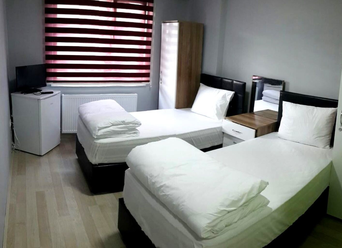 Habitació d'hotel amb dos llits, una petita taula de nit, un armari i una finestra amb persianes.