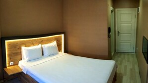Una camera da letto con testiera in legno, letto con lenzuola bianche, comodino e una porta sullo sfondo.