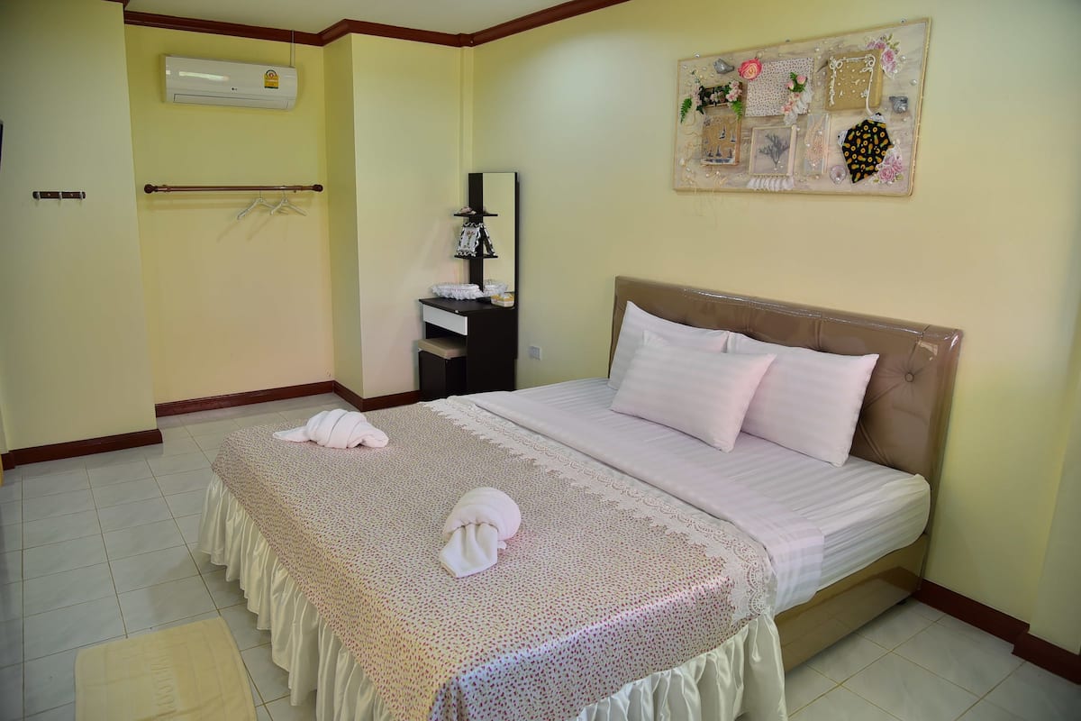 A neatly made bed with a patterned bedspread and pillows, a bedside table with a mirror and decorative items, and a wall-mounted air conditioner.