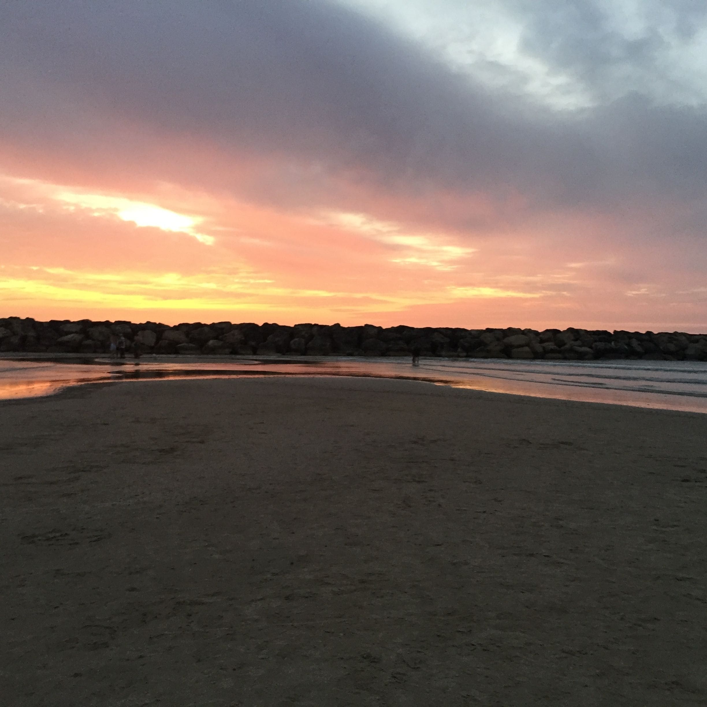 Una playa con costa rocosa y un atardecer al fondo.