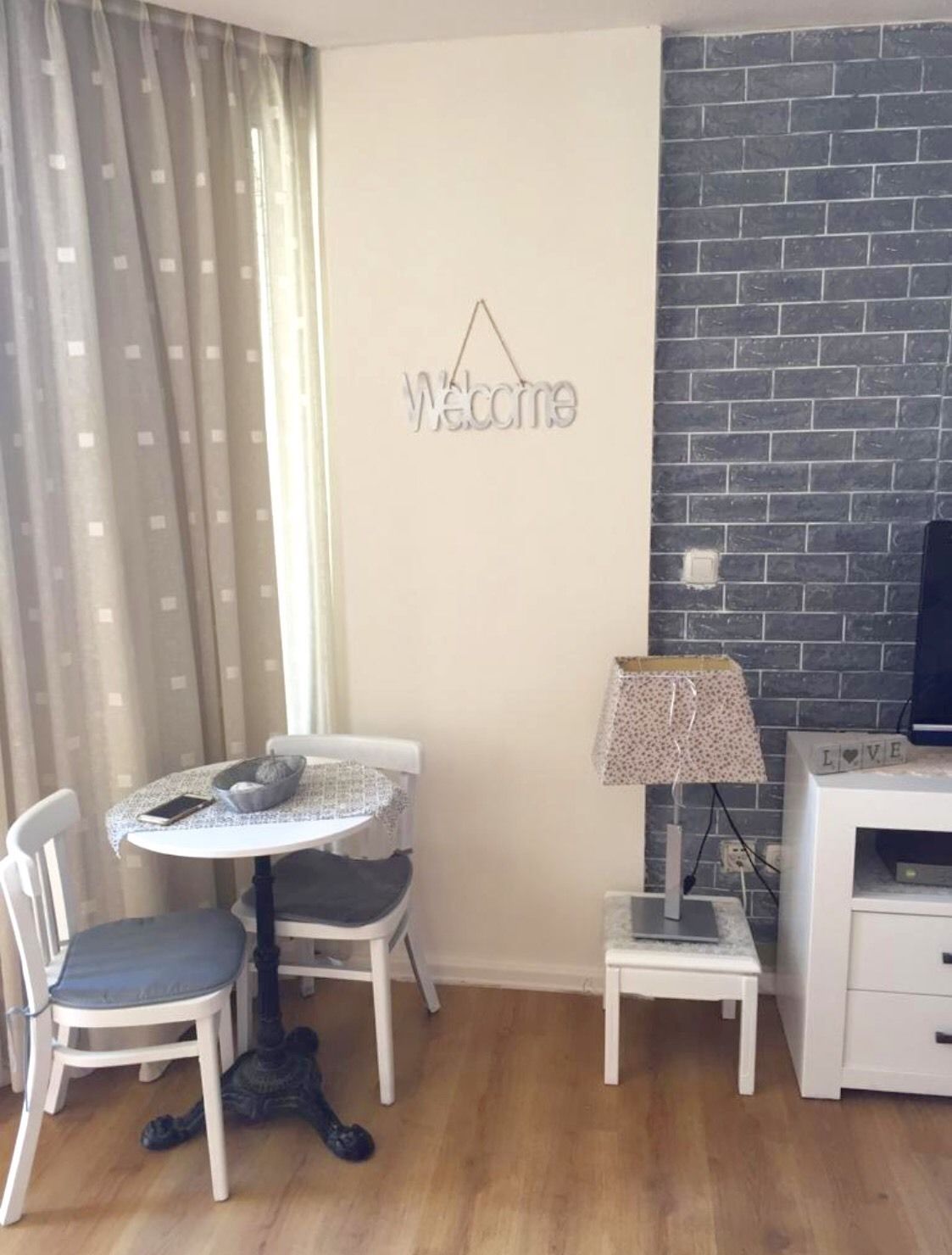Una habitación pequeña con una mesa redonda, dos sillas, una lámpara y un televisor.