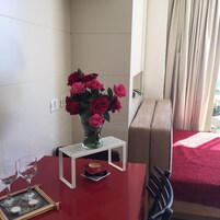 Una habitación con una mesa roja, un jarrón de rosas rojas, una vela y una pequeña bandeja con un marco de fotos.