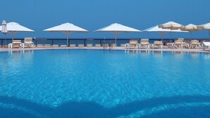 A clear blue pool with white lounge chairs and umbrellas, surrounded by a clear sky. - Raphael Apartments (Herzliya)