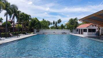 A rectangular swimming pool with clear blue water, surrounded by lounge chairs and palm trees.