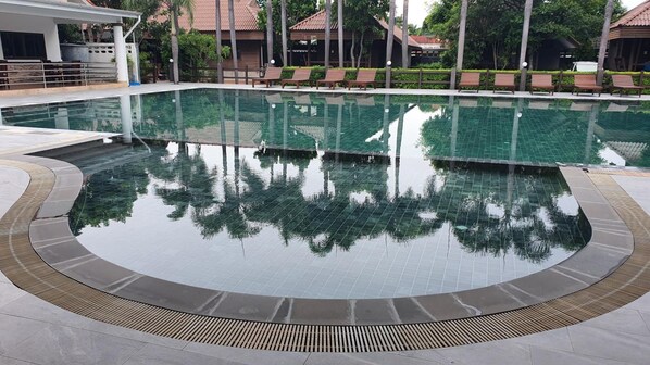 A swimming pool with a tiled edge, surrounded by lounge chairs and a wooden deck. - Pruksa Resort Prachuabkhirikhan (Prachuap Khiri Khan)