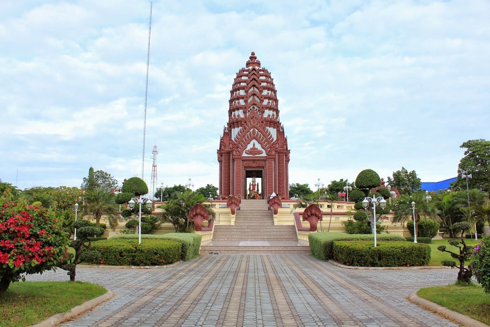 A temple with a central spire, surrounded by well-maintained gardens and a paved pathway leading to the entrance.
