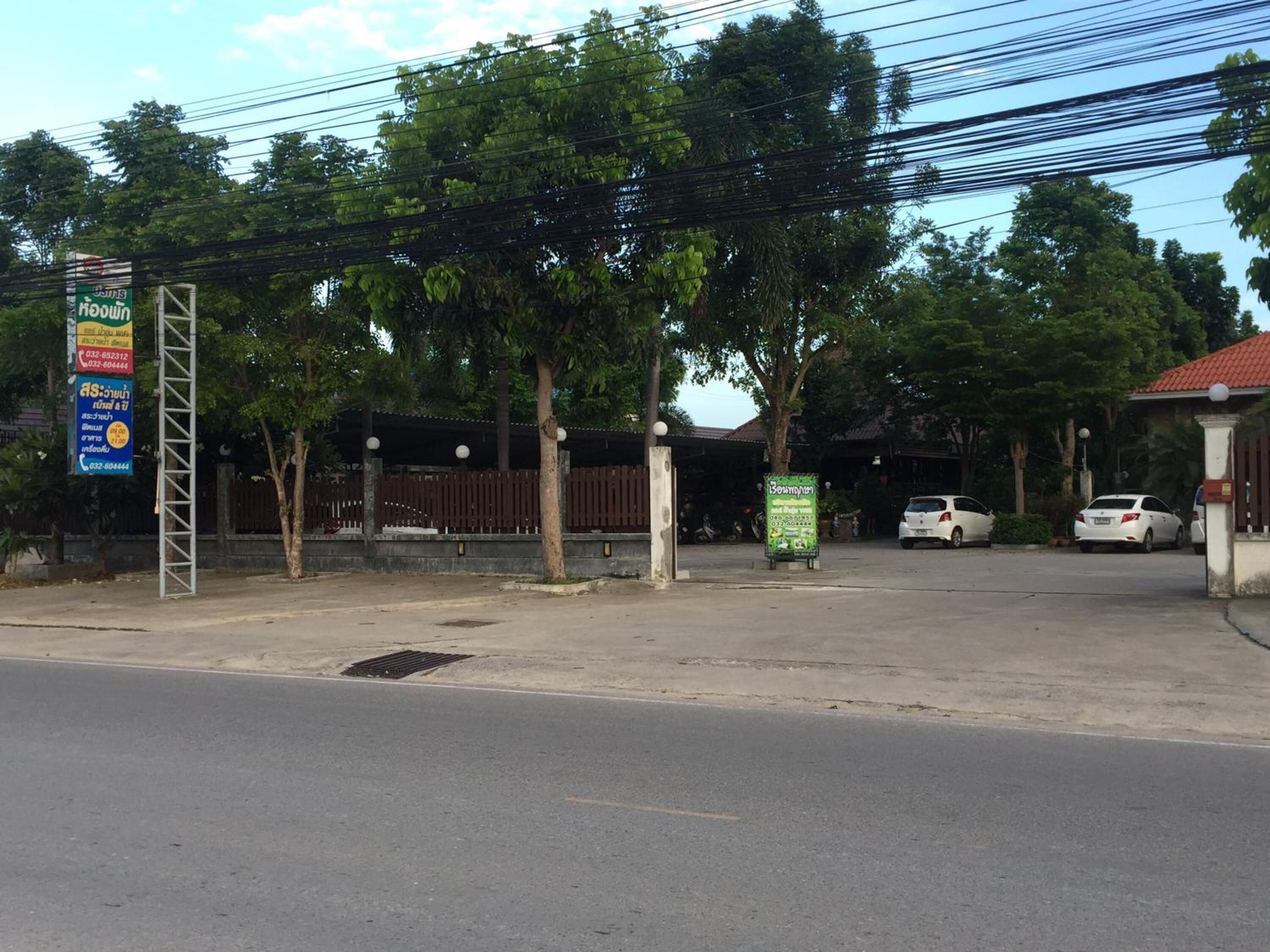 Un área de estacionamiento con acceso mediante portón, árboles y un edificio de techo rojo.